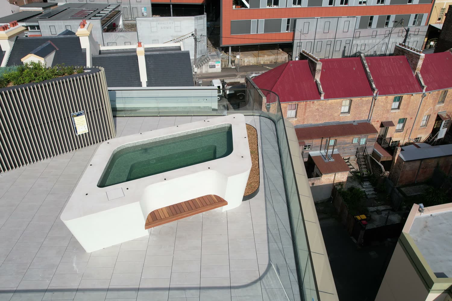 White concrete rooftop pool with timber bench seat above heritage terraces, The Rocks