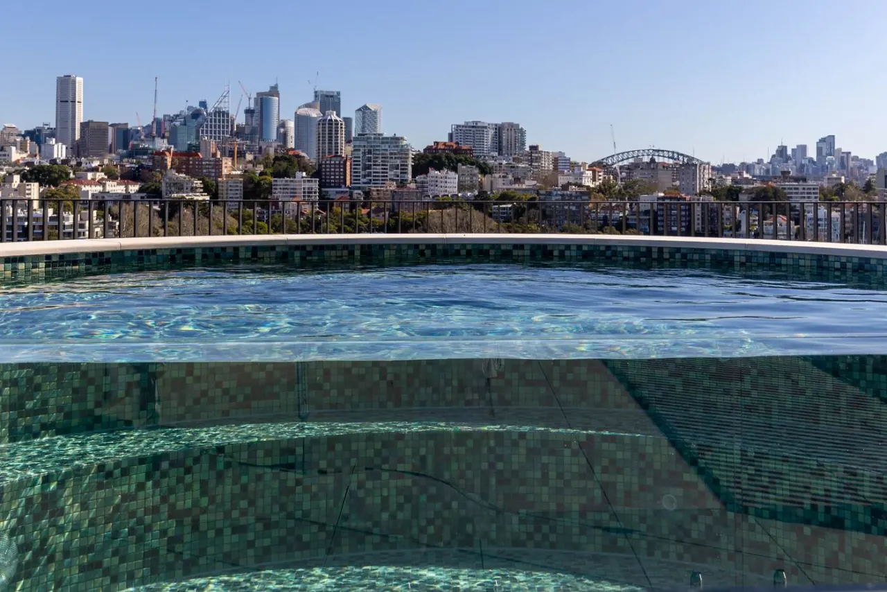 Rooftop pool water flush to the glass edge with the Sydney skyline beyond