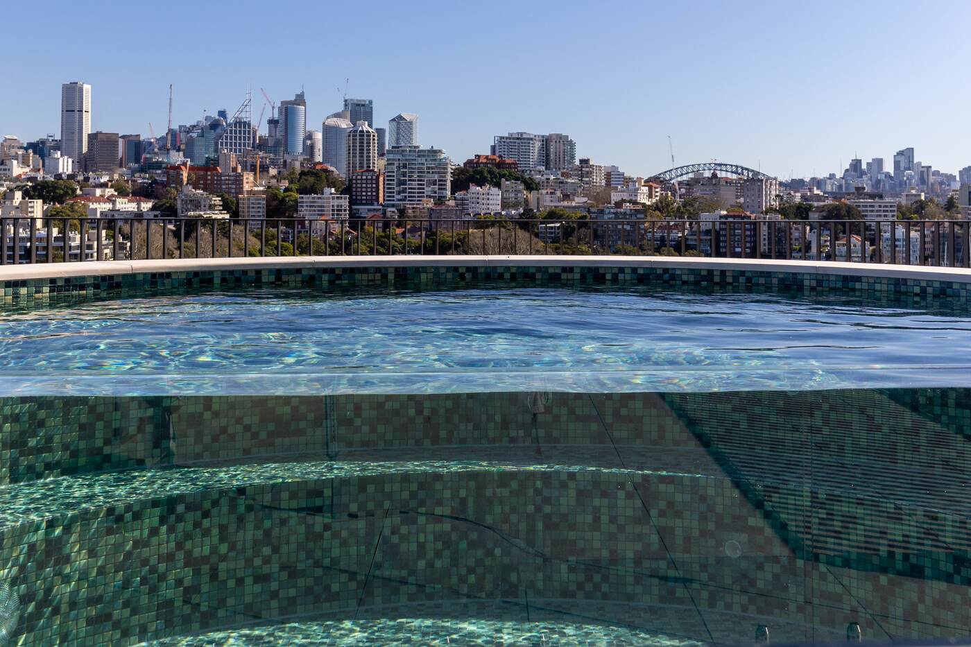 Rooftop pool water flush to the glass edge with the Sydney skyline beyond