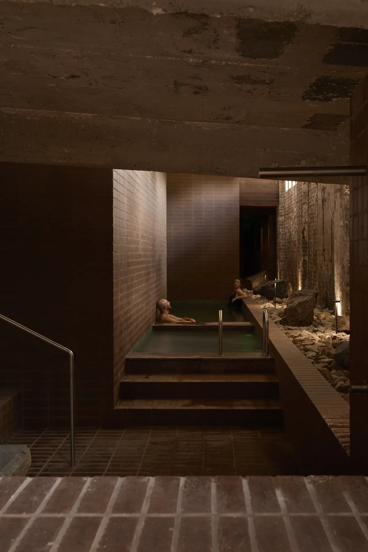 Bathers above the hot pool and cold plunge, boulders along the edge, Sense of Self